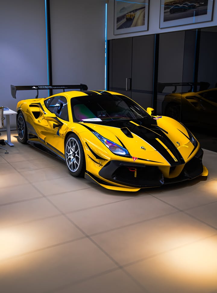 Yellow Ferrari 488 Challenge Evo with black bonnet stripes, front three-quarter angle under hard showroom spotlights.