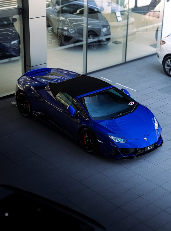 Blue Lamborghini Huracan EVO Spyder with the roof up, shot from above at a front three-quarter angle on a dealership forecourt.
