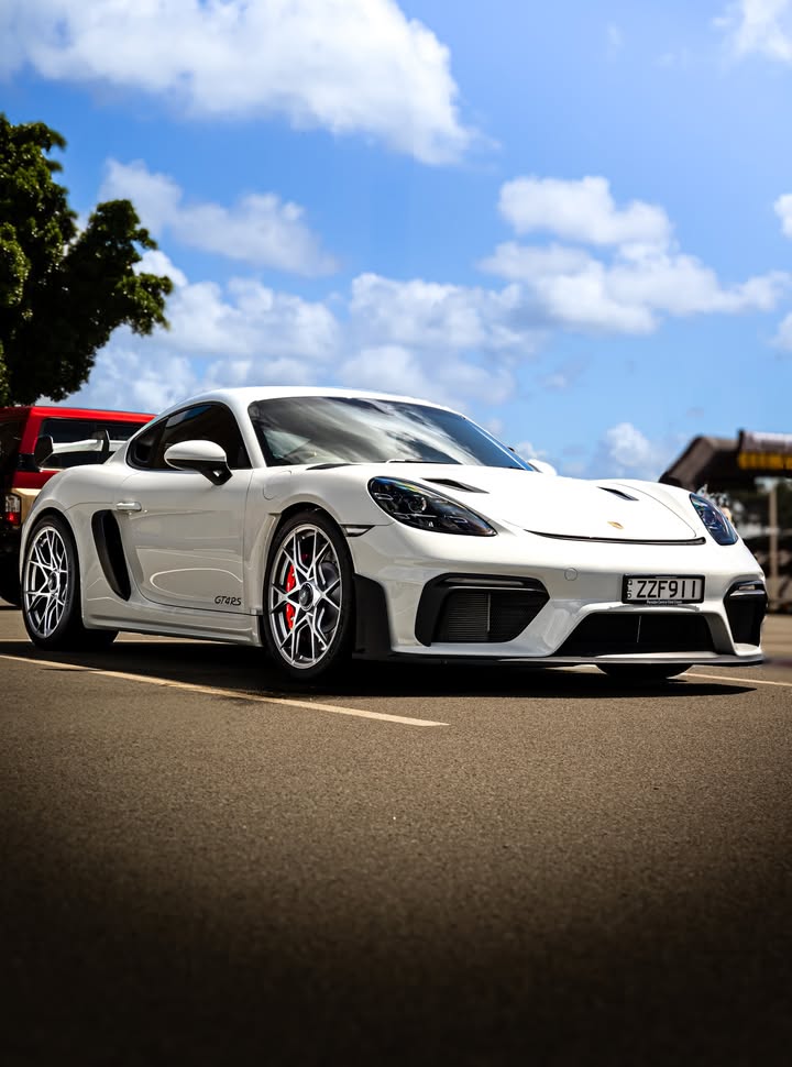 White Porsche 718 Cayman GT4 RS at a front three-quarter angle, hard midday sun and a bright blue Queensland sky behind it.