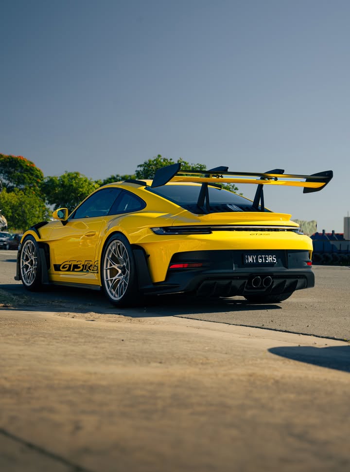 Yellow Porsche 911 GT3 RS from the rear three-quarter, swan-neck rear wing standing clear against an empty sky.
