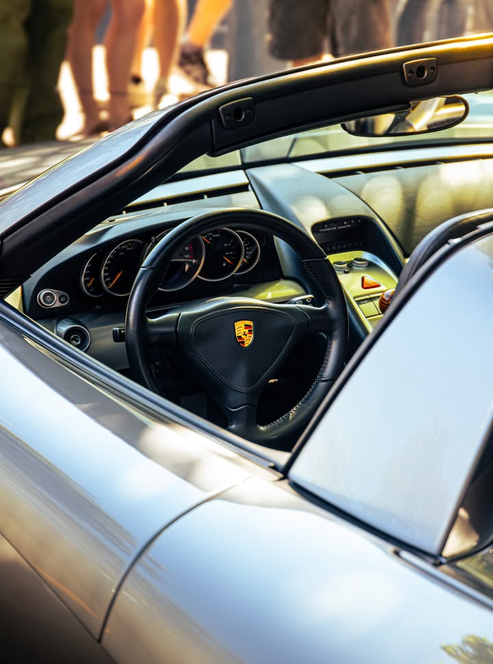Cockpit of a silver Porsche Carrera GT shot through the open roof, three-spoke wheel and analogue dials in low sun.
